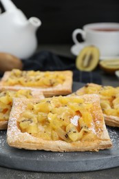 Fresh tasty puff pastry with sugar powder and kiwi on grey table, closeup