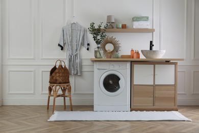 Photo of Laundry room interior with modern washing machine and stylish vessel sink on countertop