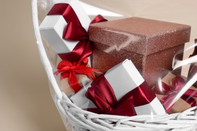 Photo of Wicker basket full of gift boxes on beige background, closeup