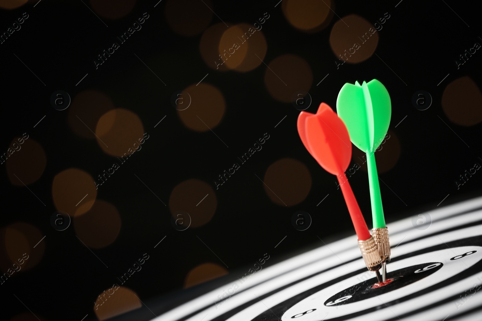 Photo of Arrows hitting target on dart board against blurred lights. Space for text