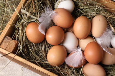 Photo of Fresh chicken eggs and dried hay in wooden crate on table, top view