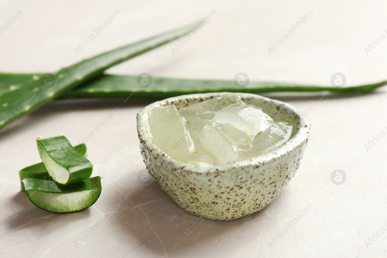 Photo of Bowl with aloe vera gel and fresh leaves on gray table