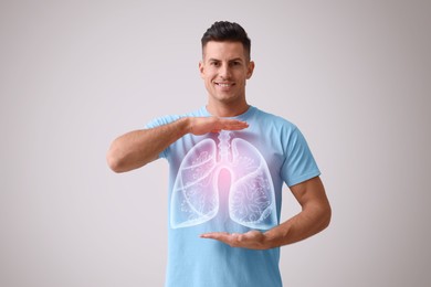 Handsome man holding hands near chest with illustration of lungs on grey background