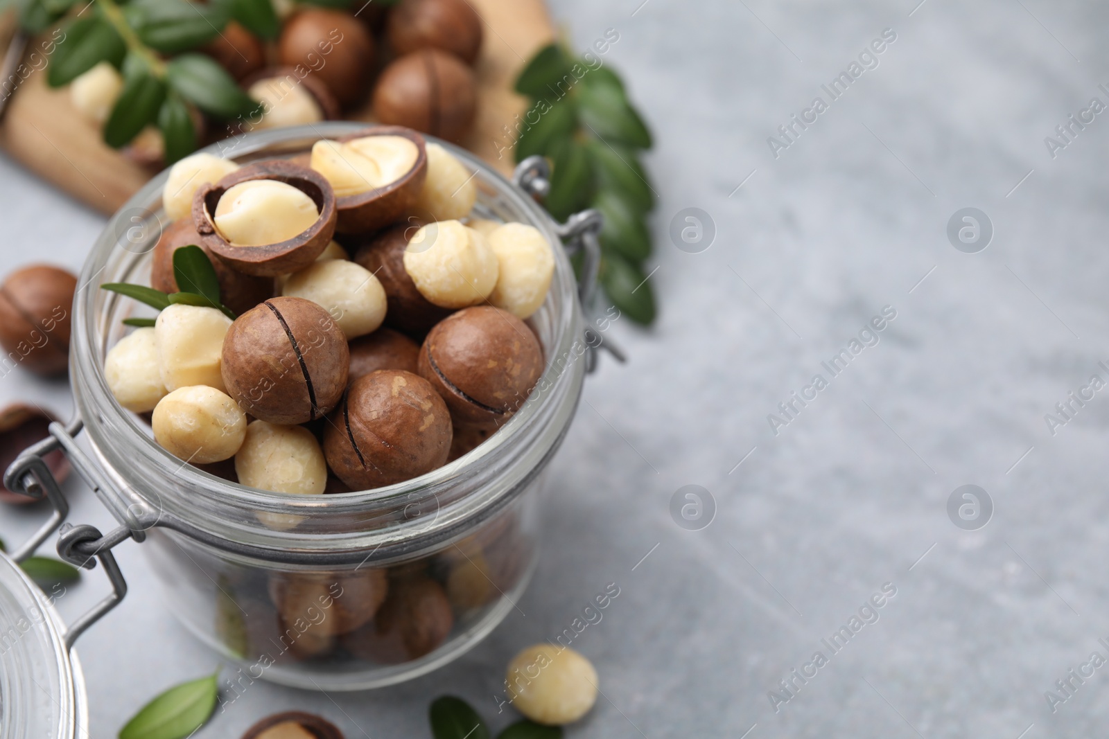 Photo of Tasty Macadamia nuts in jar on light grey table, closeup. Space for text