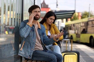 Being late. Worried couple with suitcases sitting at bus station outdoors