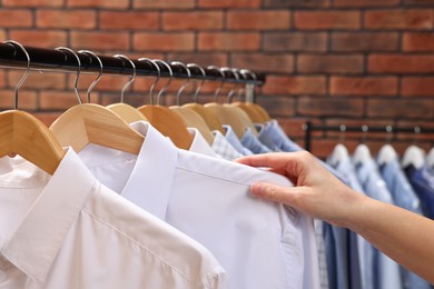 Photo of Dry-cleaning service. Woman taking shirt from rack against brick wall, closeup