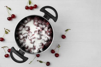 Pot with cherries and sugar on white wooden table, space for text. Making delicious jam