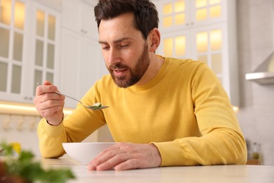 Photo of Man eating delicious chicken soup at light table in kitchen