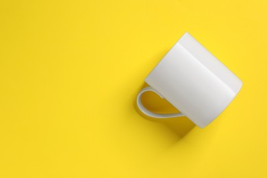 Photo of One white ceramic mug on yellow background, top view. Space for text