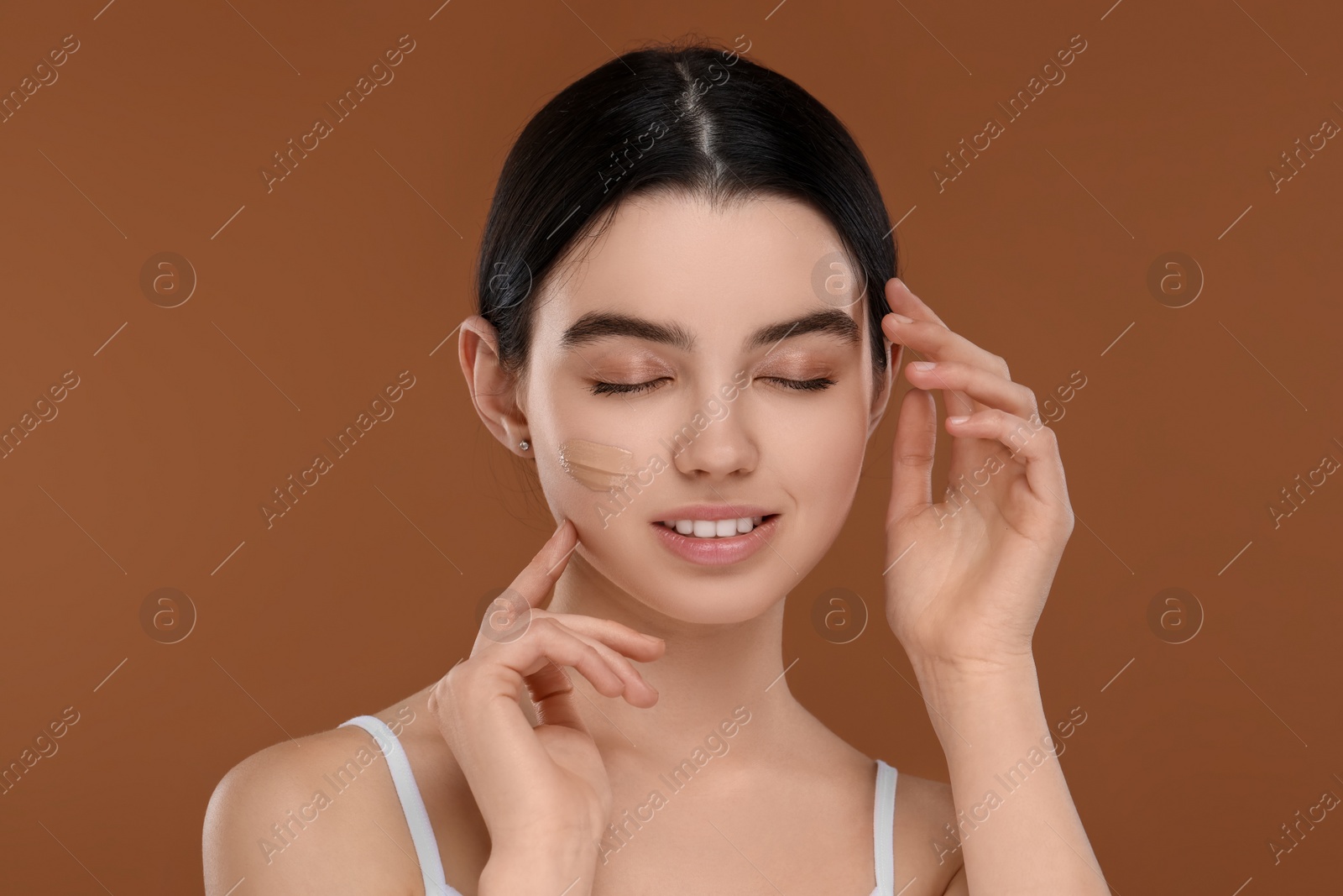 Photo of Teenage girl with swatch of foundation on face against brown background