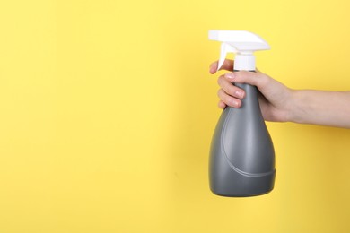 Photo of Woman holding plastic spray bottle on yellow background, closeup. Space for text