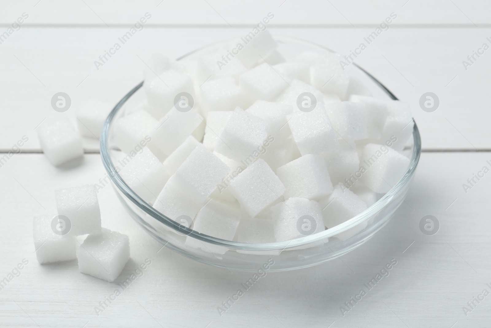 Photo of Many sugar cubes in glass bowl on white wooden table