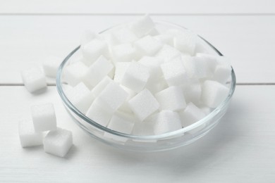 Many sugar cubes in glass bowl on white wooden table