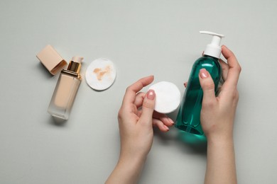 Photo of Woman with makeup remover, cotton pads and foundation on light grey background, top view