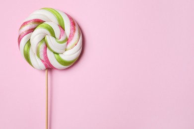 Photo of Stick with colorful lollipop swirl on pink background, top view. Space for text