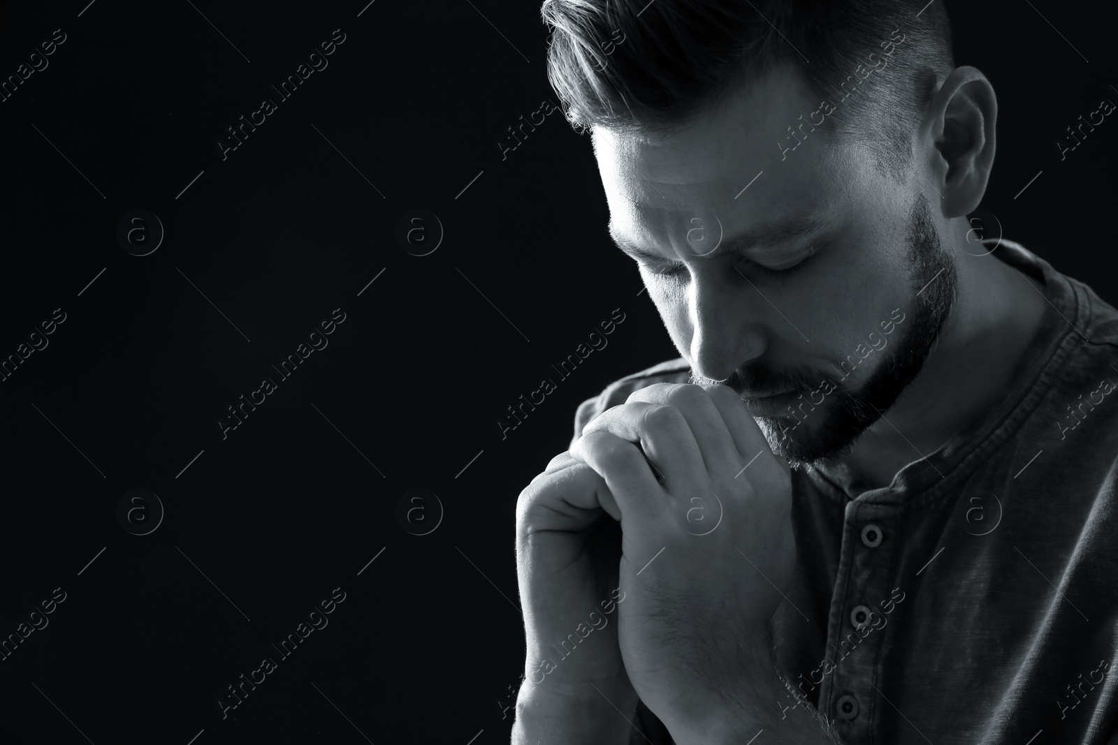 Photo of Man with hands clasped together for prayer on dark background, black and white effect. Space for text