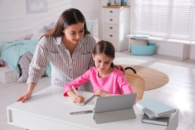 Mother helping her daughter doing homework with tablet at home