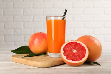 Photo of Tasty grapefruit juice in glass and fresh fruits on light wooden table