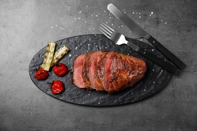 Board with slices of grilled meat on grey table, top view