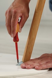 Photo of Man with screwdriver assembling furniture on floor indoors, closeup