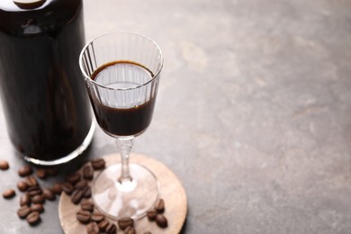 Bottle of coffee liqueur, shot glass and beans on light grey table, closeup. Space for text