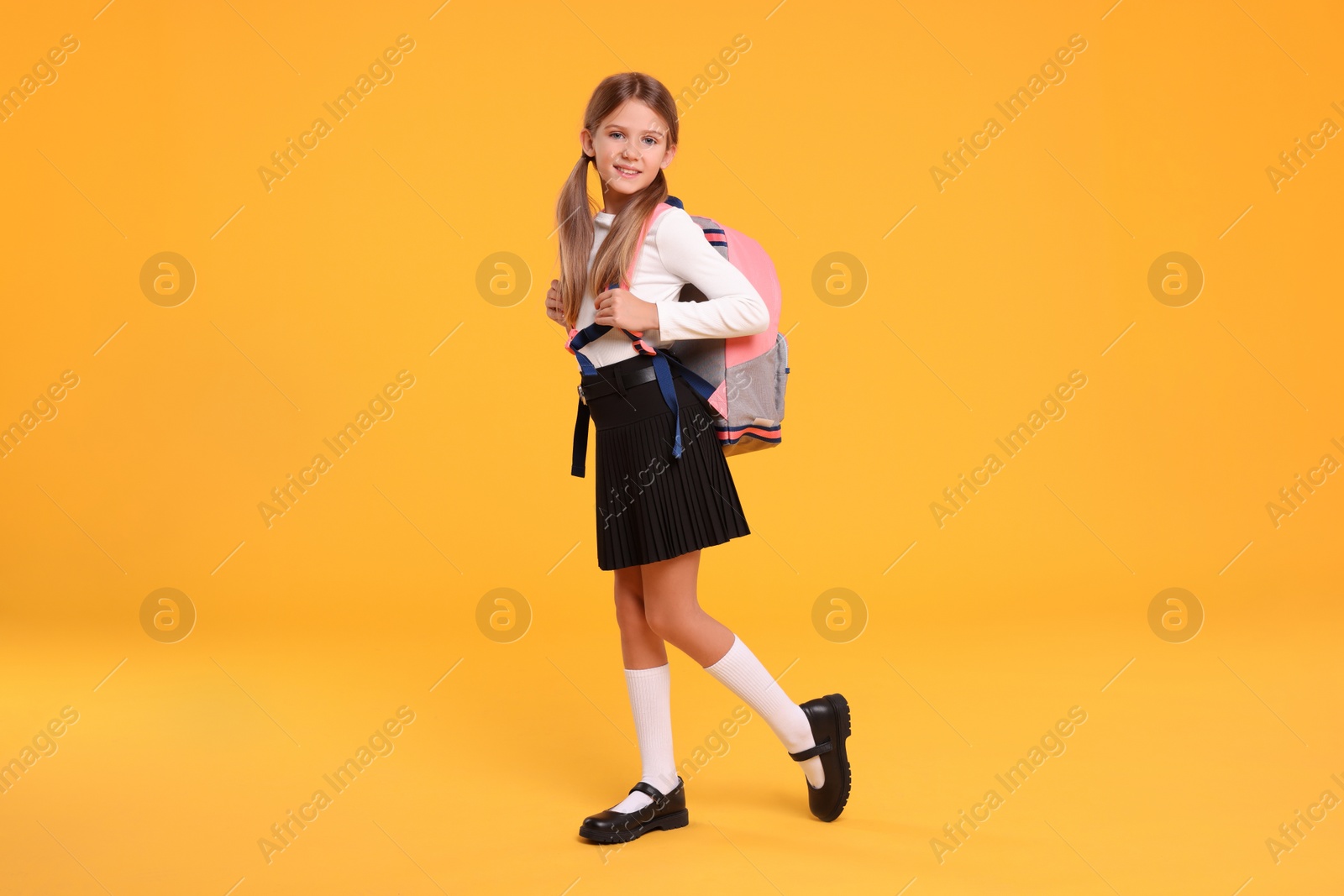 Photo of Happy schoolgirl with backpack on orange background