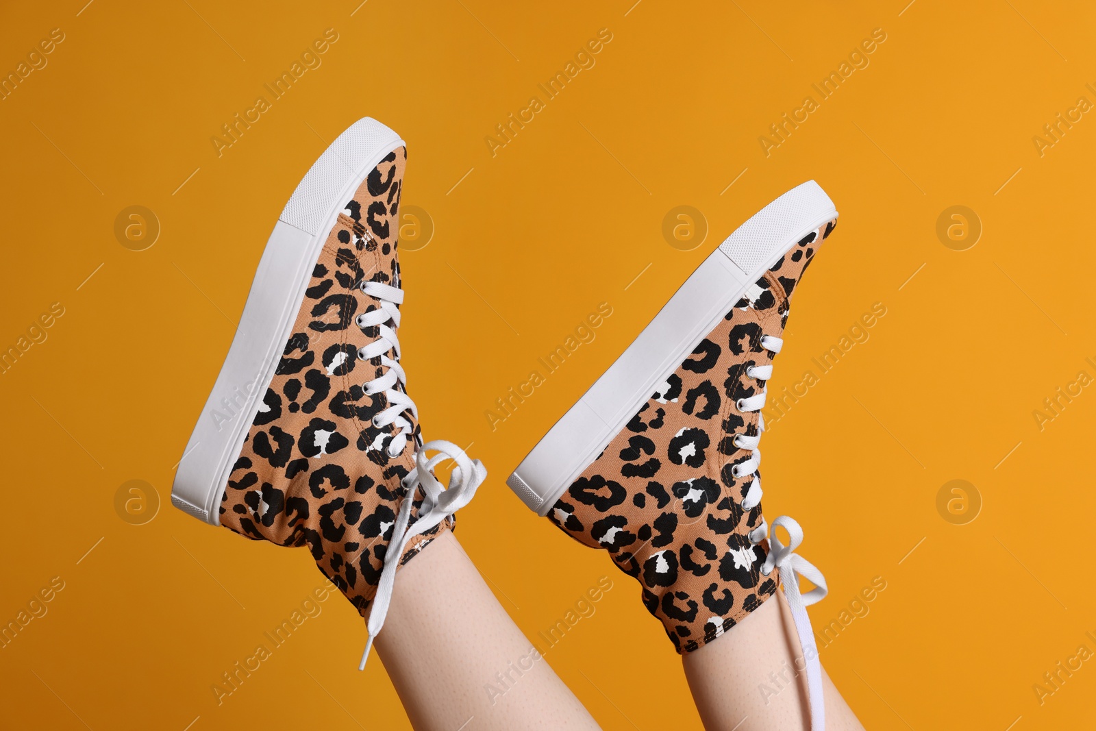 Photo of Woman posing in classic old school sneakers with leopard print on orange background, closeup