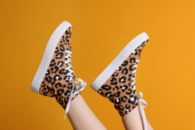 Photo of Woman posing in classic old school sneakers with leopard print on orange background, closeup