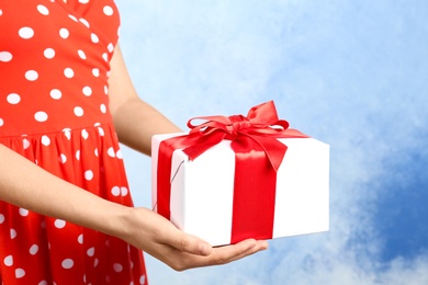 Photo of Woman holding beautifully wrapped gift box on color background