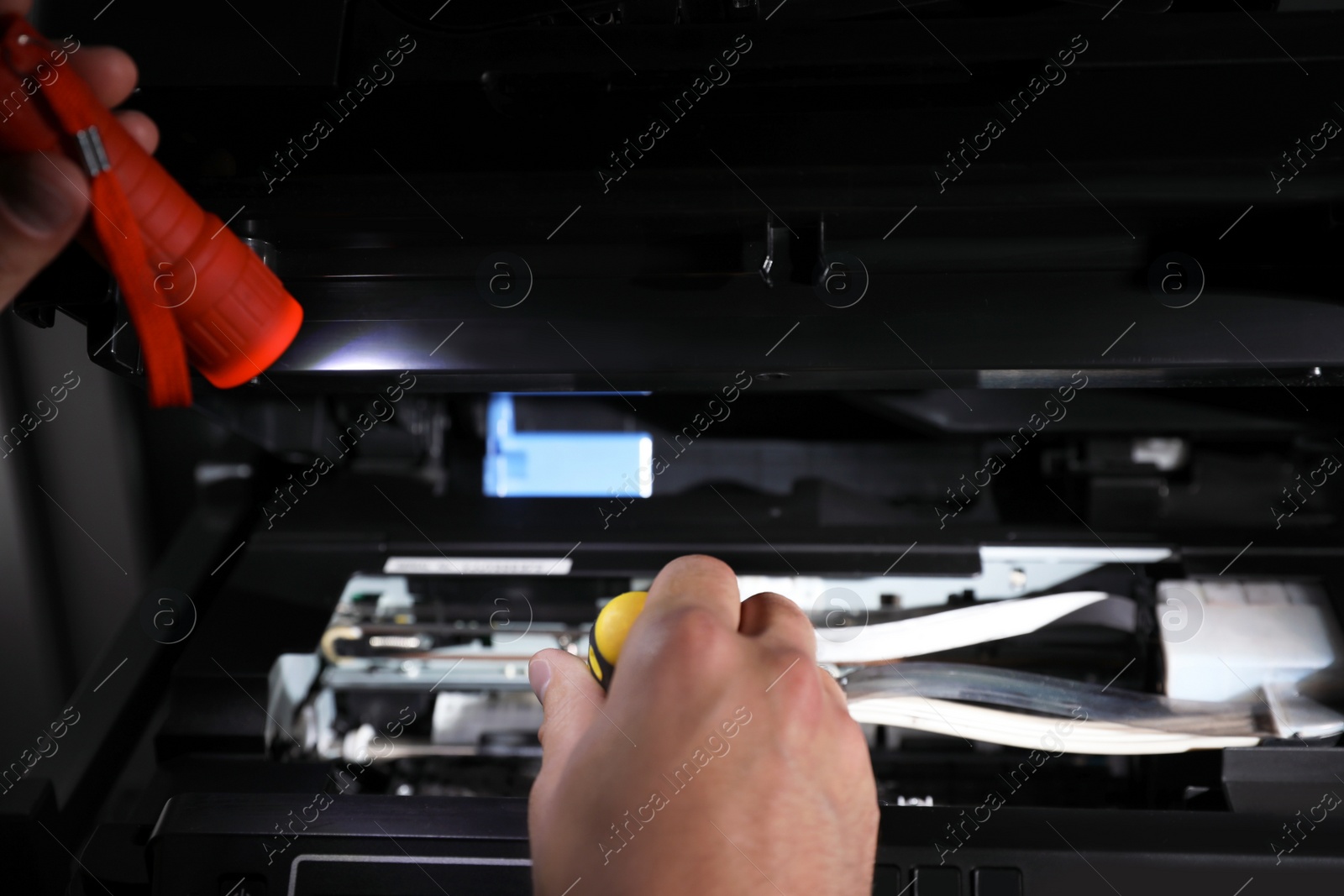 Photo of Repairman with flashlight fixing modern printer indoors, closeup