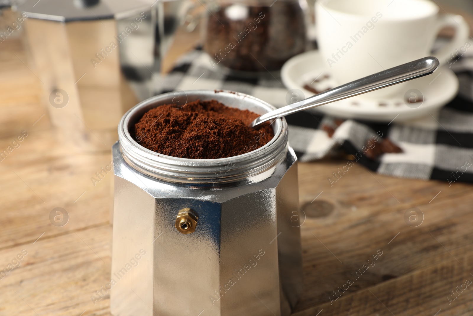 Photo of Moka pot and spoon with ground coffee on wooden table, closeup