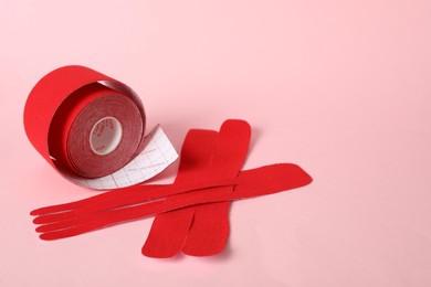 Photo of Red kinesio tape roll and pieces on pink background, space for text