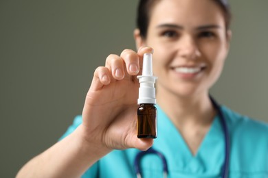 Woman holding nasal spray bottle on olive background, selective focus