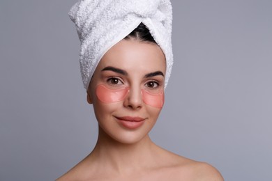 Photo of Beautiful young woman with under eye patches and hair wrapped in towel on grey background