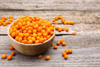 Bowl with fresh ripe sea buckthorn berries on wooden table, space for text