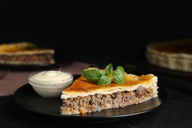 Photo of Piece of delicious pie with minced meat, basil and sauce served on black table, closeup