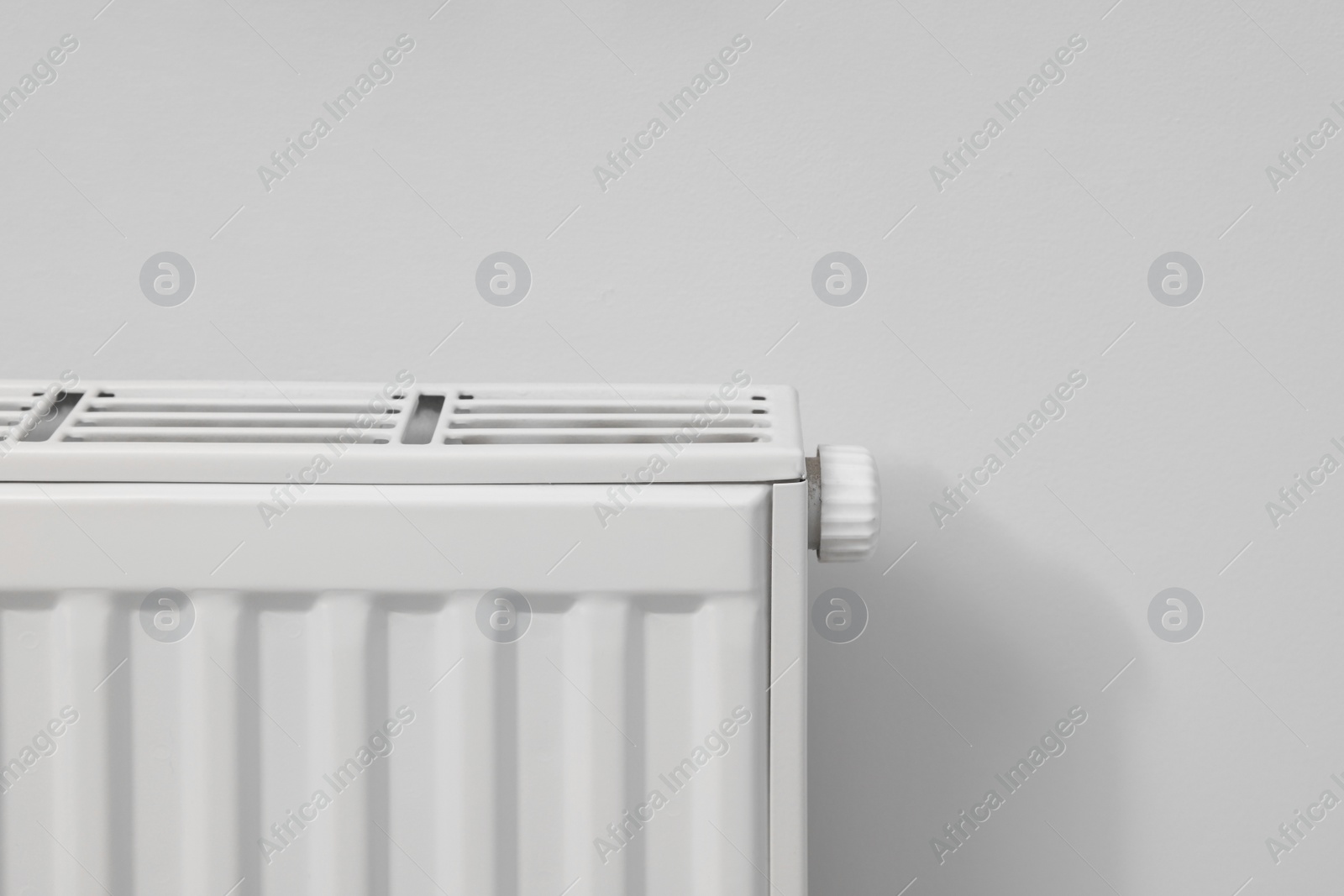 Photo of Modern radiator on white wall, closeup. Space for text