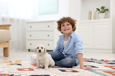 Photo of Little boy with cute puppy on carpet at home