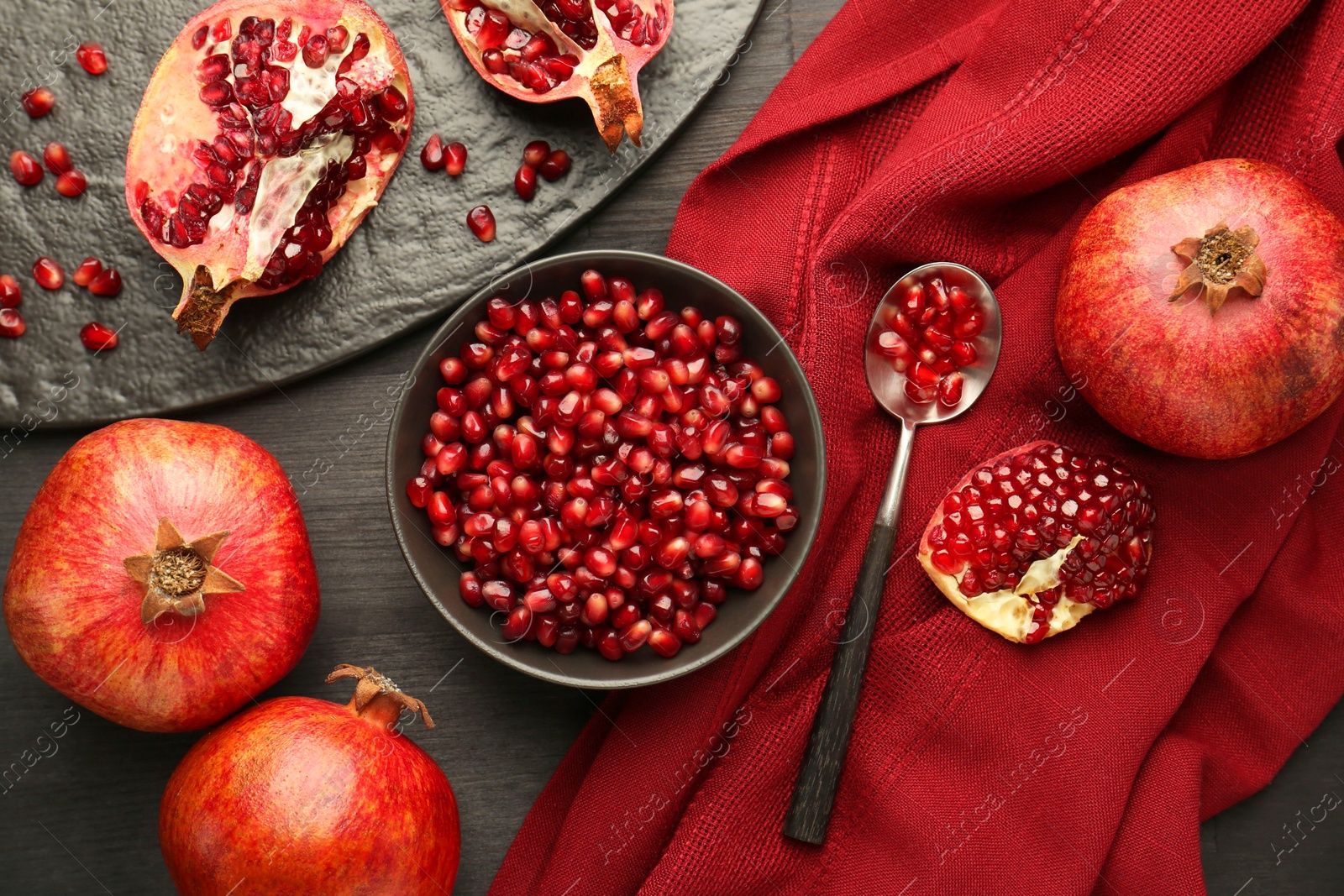 Photo of Tasty ripe pomegranates and grains on dark wooden table, flat lay