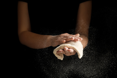 Woman preparing dough for pizza on black background, closeup