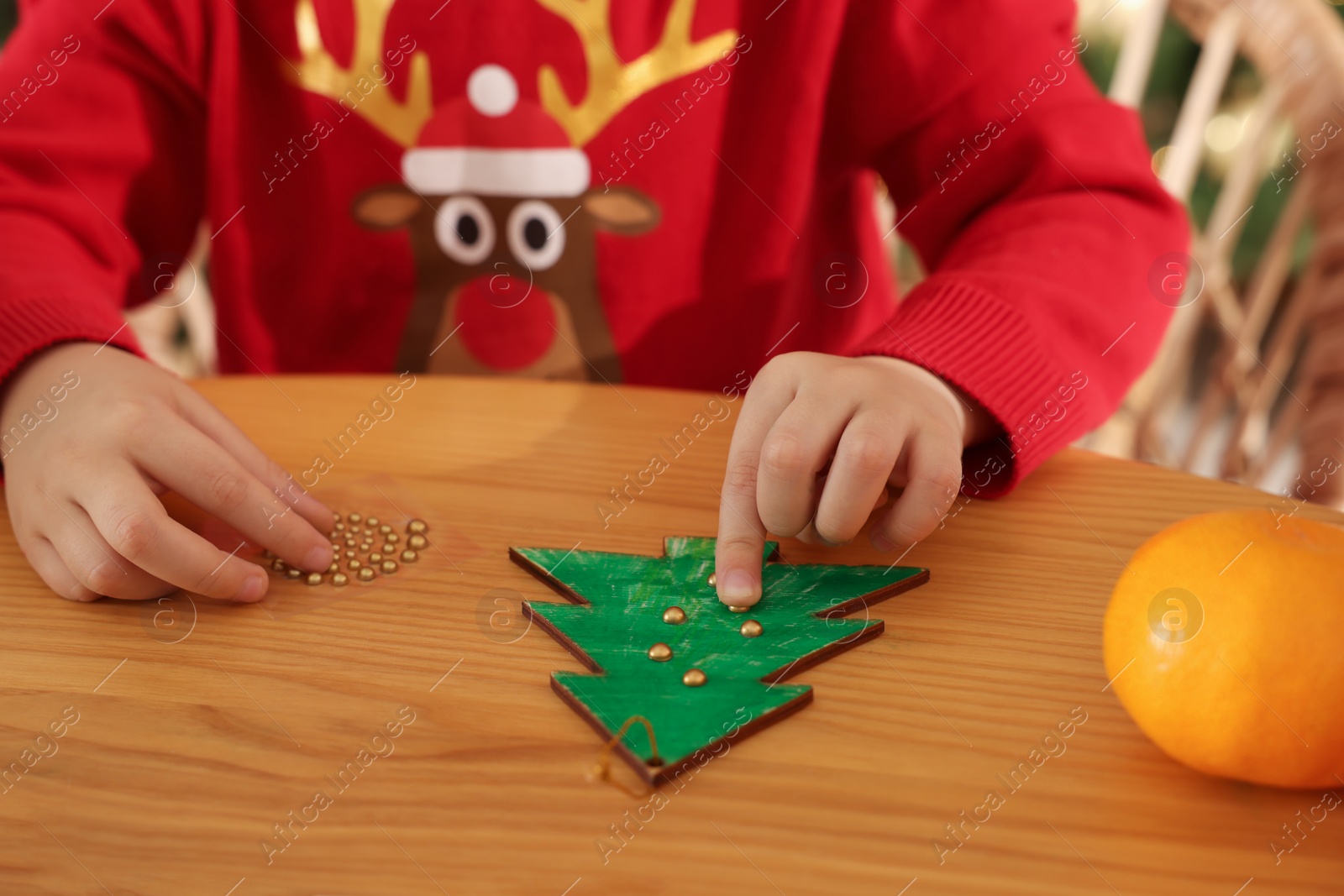 Photo of Little child making Christmas tree craft at wooden table, closeup