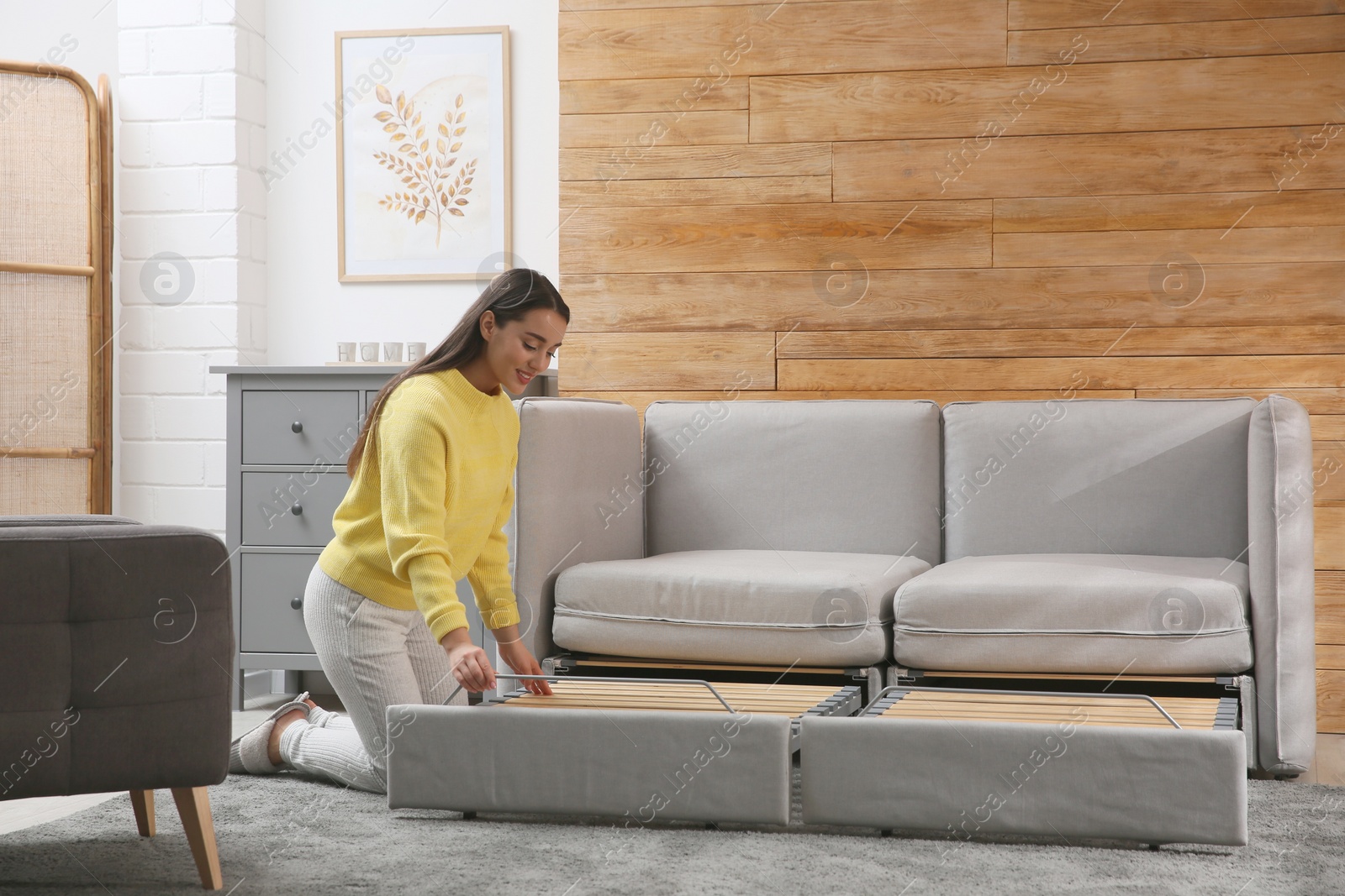 Photo of Young woman unfolding sofa into a bed in room. Modern interior