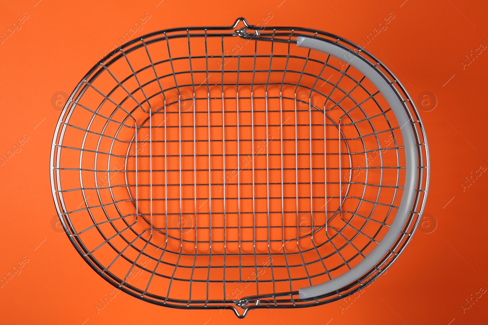 Photo of Empty metal shopping basket on orange background, top view