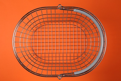 Empty metal shopping basket on orange background, top view