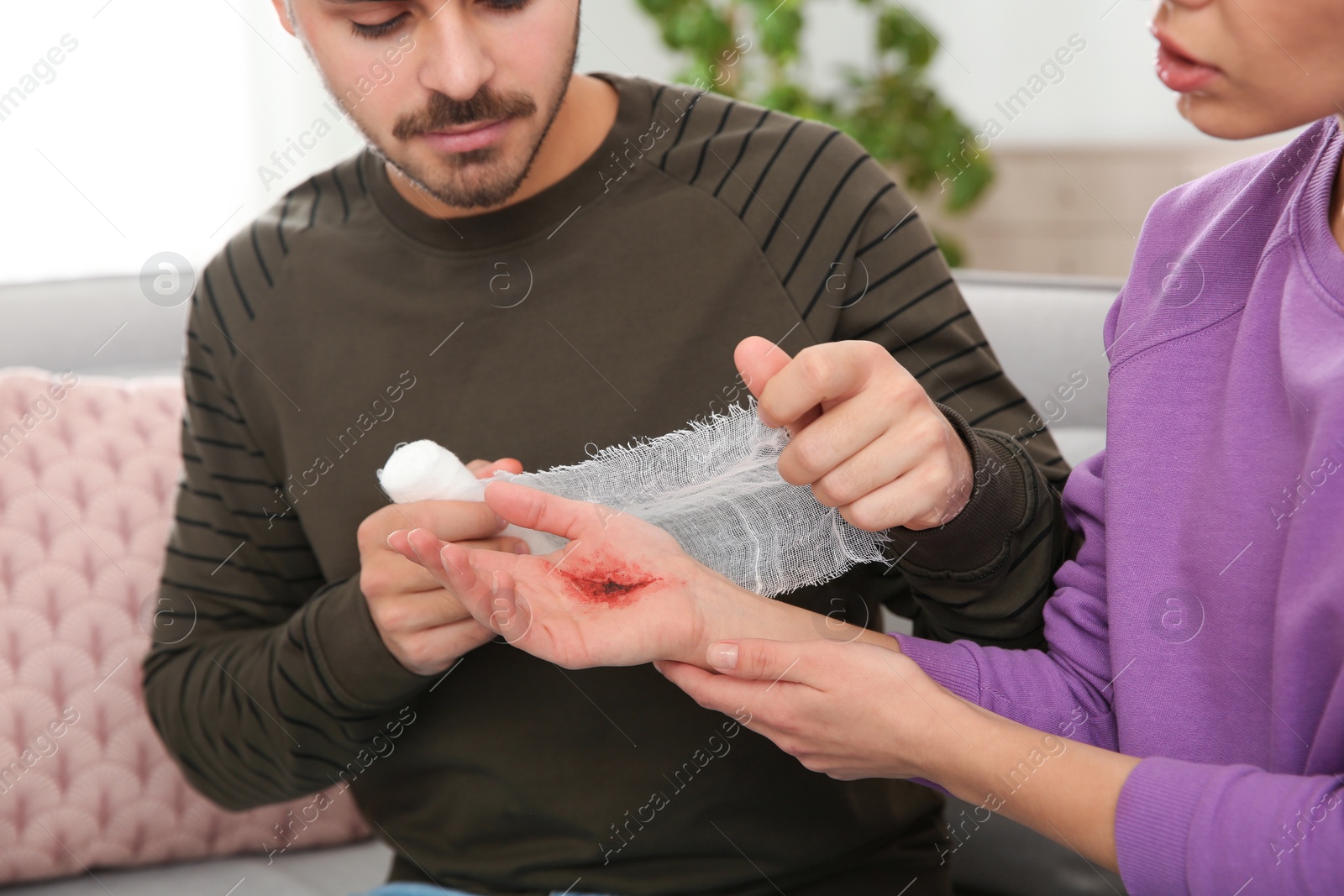 Photo of Young man applying bandage on woman's injured hand at home, closeup. First aid