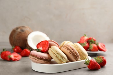 Photo of Delicious macarons, strawberries and coconut on grey table