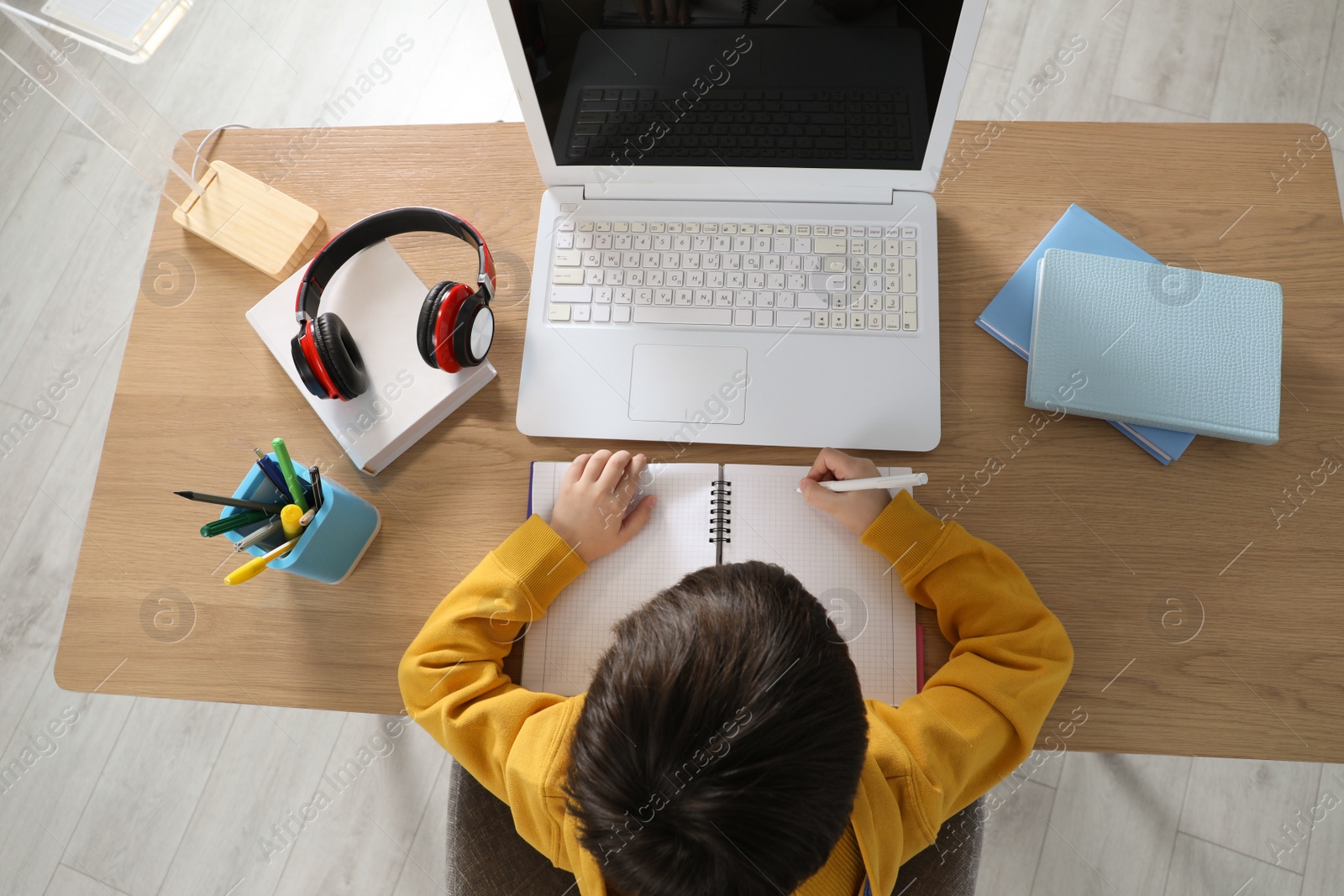 Photo of Cute little boy with modern laptop studying online at home, top view. E-learning