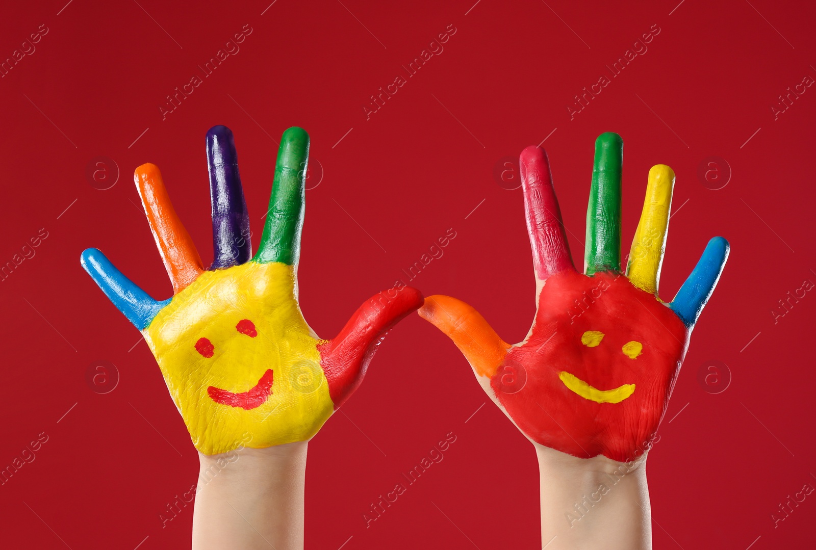 Photo of Kid with smiling faces drawn on palms against red background, closeup