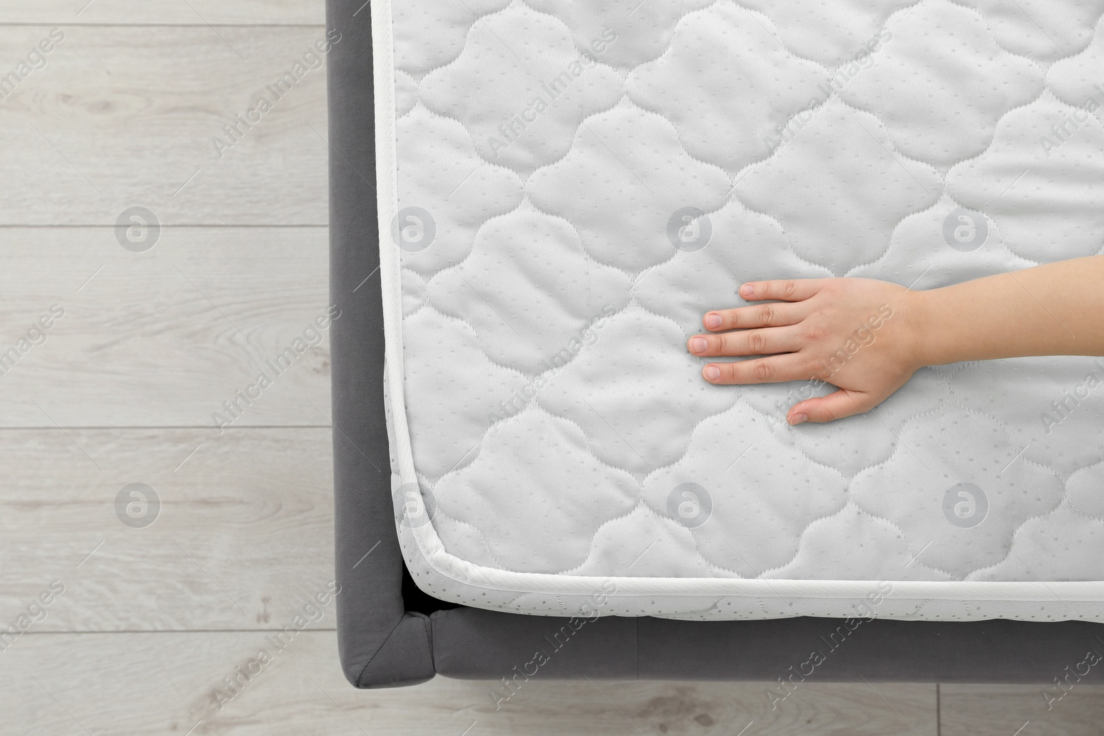 Photo of Woman touching soft light green mattress on bed, top view