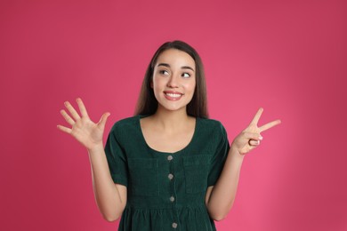 Photo of Woman showing number seven with her hands on pink background